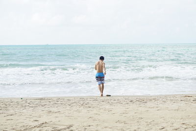 Rear view of shirtless man on beach against sky