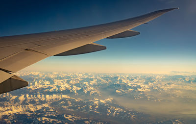 Wing of plane over mountain cover with white snow. airplane flying on blue sky. scenic view.