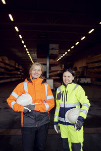 Portrait of smiling female coworkers in reflective clothing standing in lumber industry