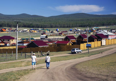 Rear view of people walking on road by houses against sky