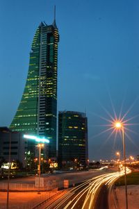 Light trails on road amidst illuminated buildings against sky at night