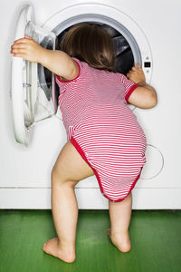 Rear view of baby girl peeking into washing machine at home