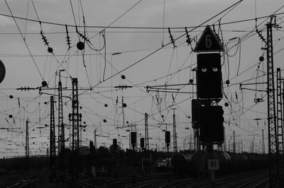 Electricity pylons by railroad tracks against sky