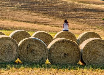 Rear view of woman on hay bales on field