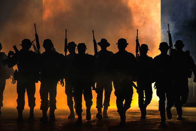 Rear view of silhouette special forces soldiers walking with guns and smoke over light background 