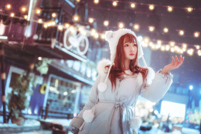 Portrait of young woman standing against illuminated lights