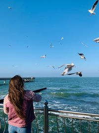 Rear view of woman looking at seascape with seagulls against sky