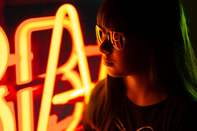 Close-up of young woman wearing sunglasses at illuminated nightclub