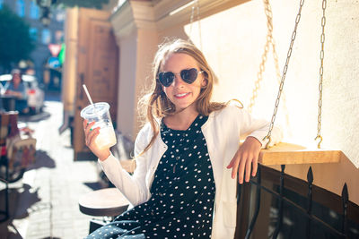 Portrait of smiling young woman holding sunglasses