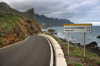 Information sign by mountain road against sea