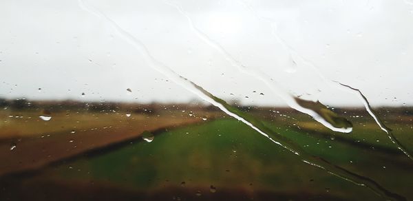 Close-up of wet window against sky