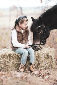 Cute girl looking at horse while sitting on hay