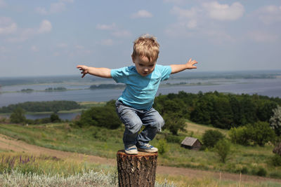 Full length of boy standing on tree trunk against landscape