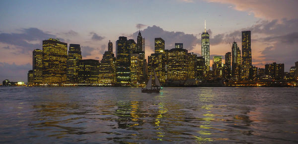 Illuminated modern buildings by sea against sky