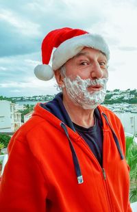 Portrait of senior man wearing santa hat standing against sky