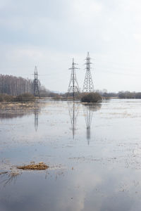 Electricity pylon by lake against sky