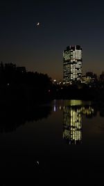 Illuminated buildings by lake against sky at night