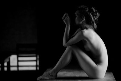 Side view of naked woman sitting on table