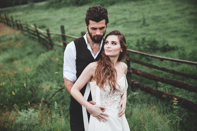 Wedding couple looking away while standing on field