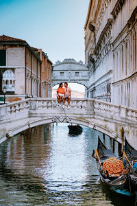 People in canal amidst buildings against sky