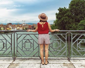 Full length of young woman standing by railing against sky