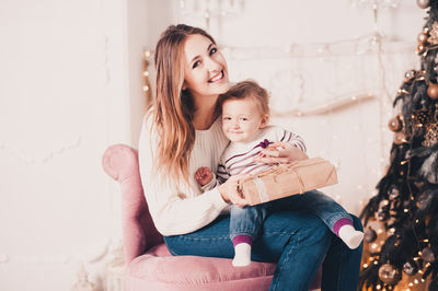 Smiling mother and daughter holding gift box at home