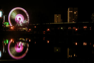 Illuminated spinning ferris wheel reflecting in river at night