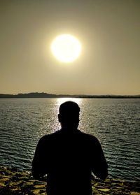 Silhouette man standing by sea against clear sky during sunset