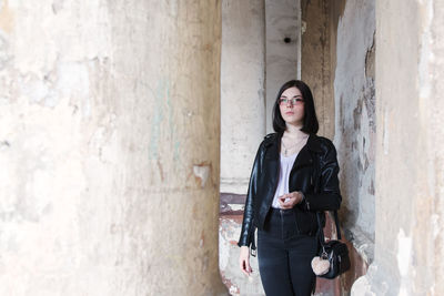 Young woman looking away while standing against wall