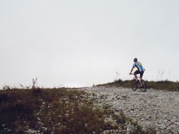 Rear view of man riding bicycle on dirt road against clear sky