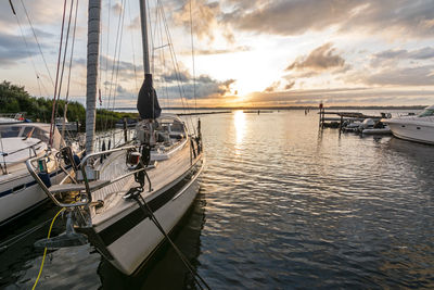 Boats moored in harbor at sunset