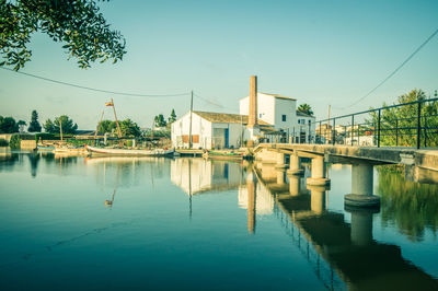 Bridge over river by buildings against sky