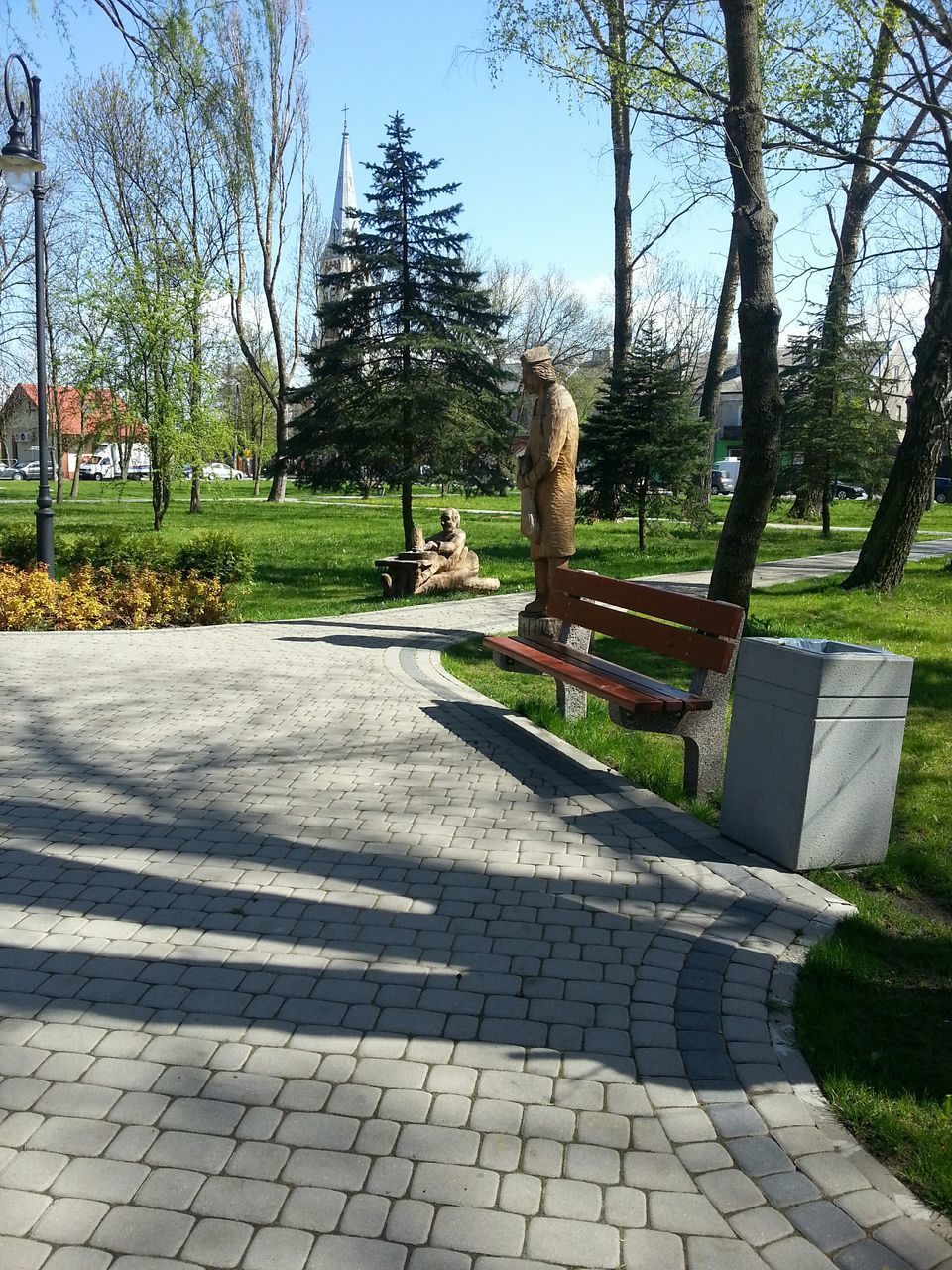 tree, grass, park - man made space, footpath, shadow, growth, sunlight, cobblestone, park, empty, bench, paving stone, tranquility, day, sky, nature, green color, lawn, outdoors, walkway