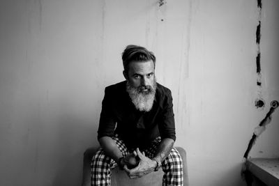 Portrait of young man sitting against wall