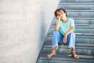 Full length of smiling girl sitting on staircase against wall