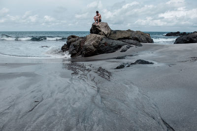 Man sitting on rocks at calm beach