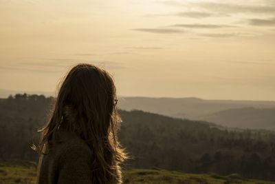 Side view of woman standing against mountains during sunset