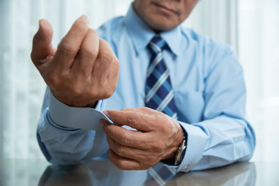 Midsection of businessman buttoning sleeve at desk