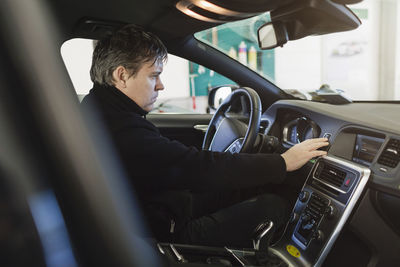 Side view of mechanic examining dashboard in car