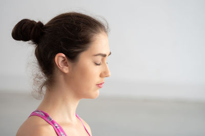 Young woman meditating while sitting against wall