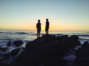 Silhouettes of two boys standing on seaside rock