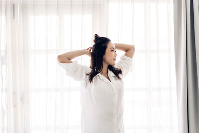 Beautiful young woman standing by window in white