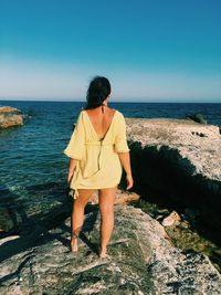 Rear view of woman standing on rock by sea against sky