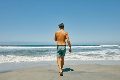 Rear view of shirtless man standing on beach