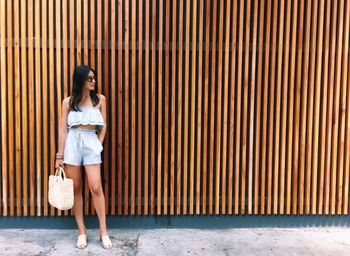 Young woman standing against wooden fence