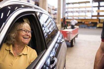 Happy female customer sitting in car looking at sales staff in hardware store