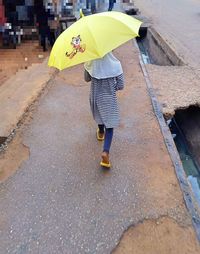 Full length rear view of woman walking on wet street during monsoon