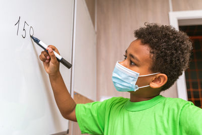 Close-up of boy wearing mask writing on whiteboard