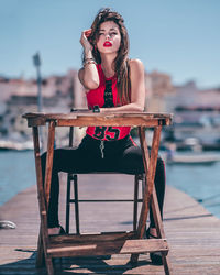 Young woman looking away while sitting on pier over sea