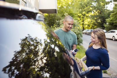 Happy couple standing by electric car